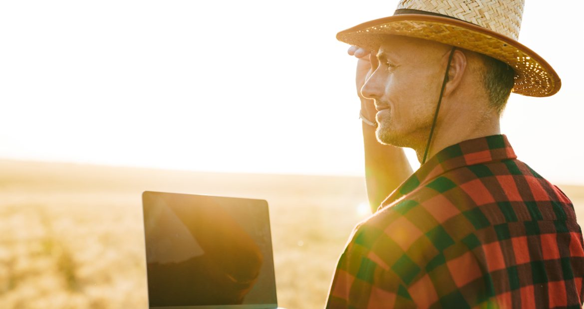 Image of adult man working with laptop while standing at cereal field Image of adult man working with laptop while standing at cereal field